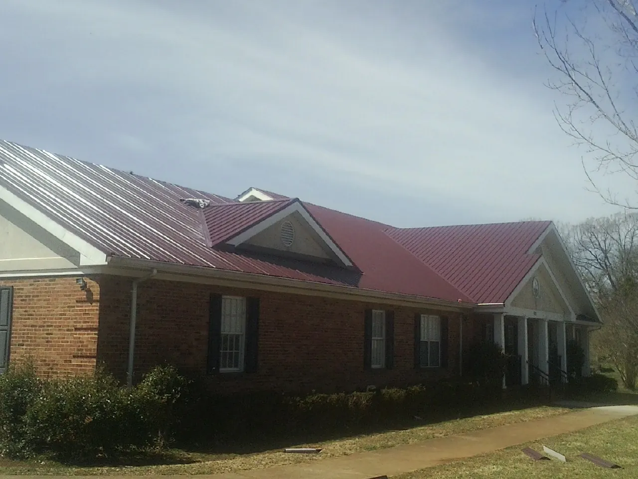 Red metal roof with gabled entries on a long brick building, from a Hail Damage Roof Repair job in Westernport