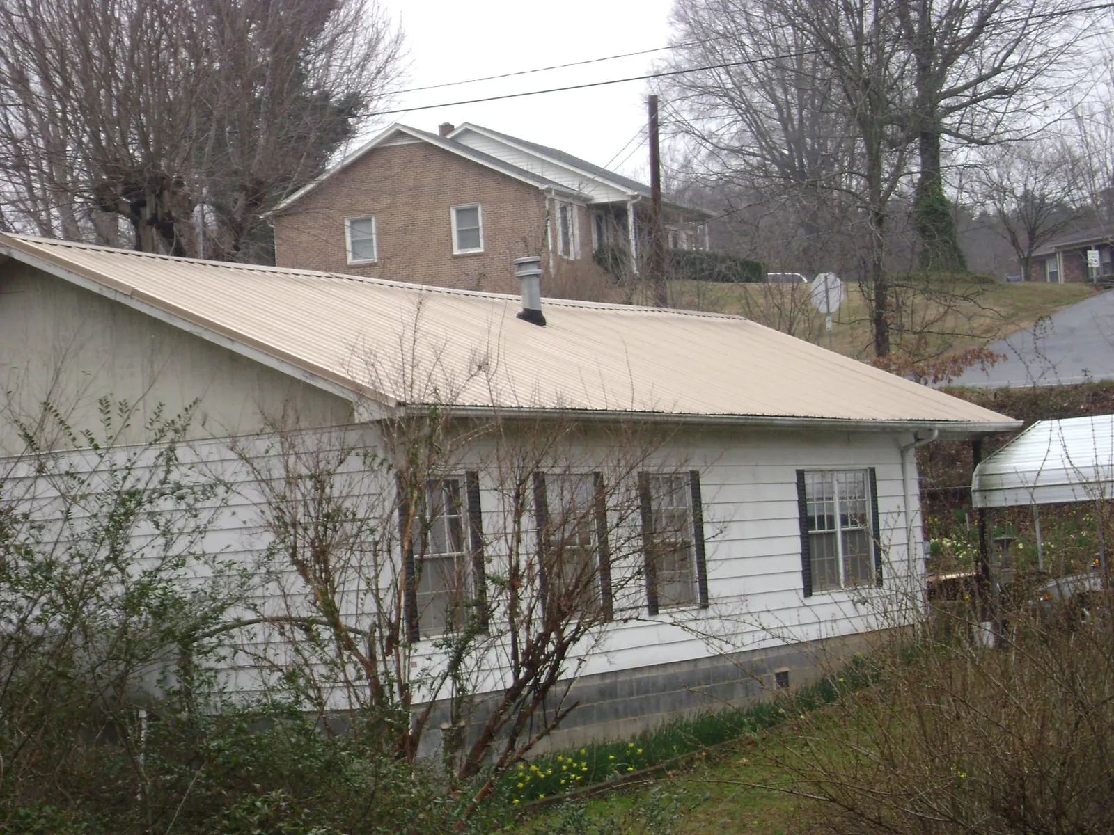 Tan metal roof on a white sided house set into a hillside — Commercial Roofing by Roofing Brothers in Westernport